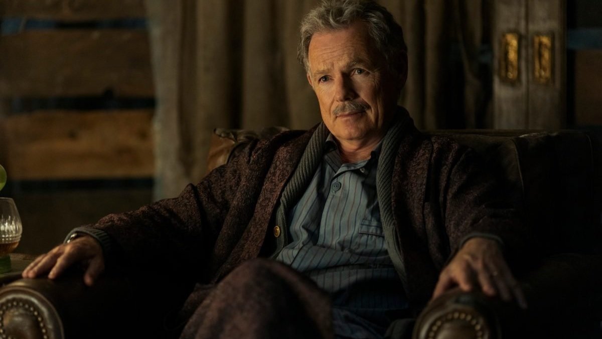 Bruce Greenwood with a mustache sits in a chair in pjs in The Fall Of The House Of Usher.