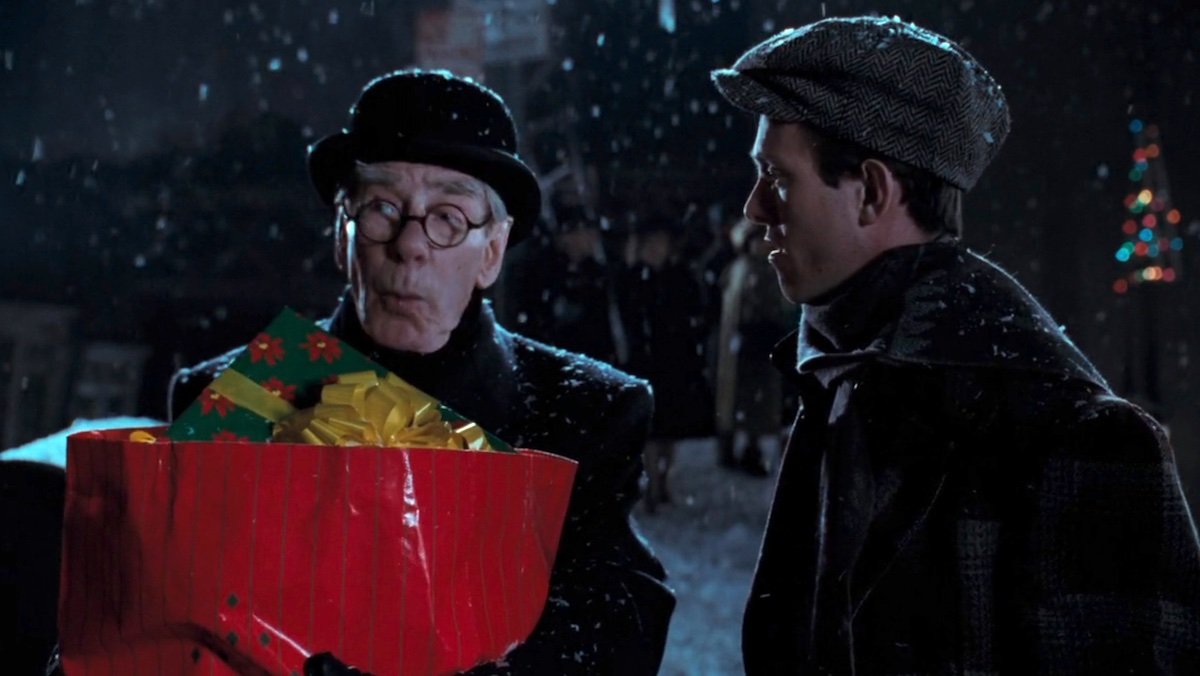 Alfred looks shocked carrying presents in the snow while talking to a newspaper salesman in Batman Returns