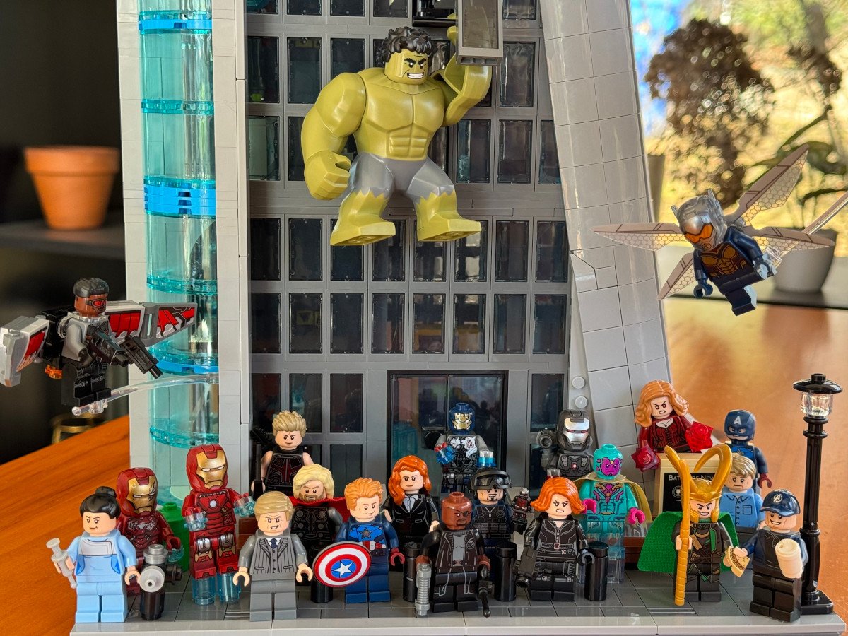 LEGO Marvel minifigs crowded in front of Avengers Tower with Hulk hanging off the front