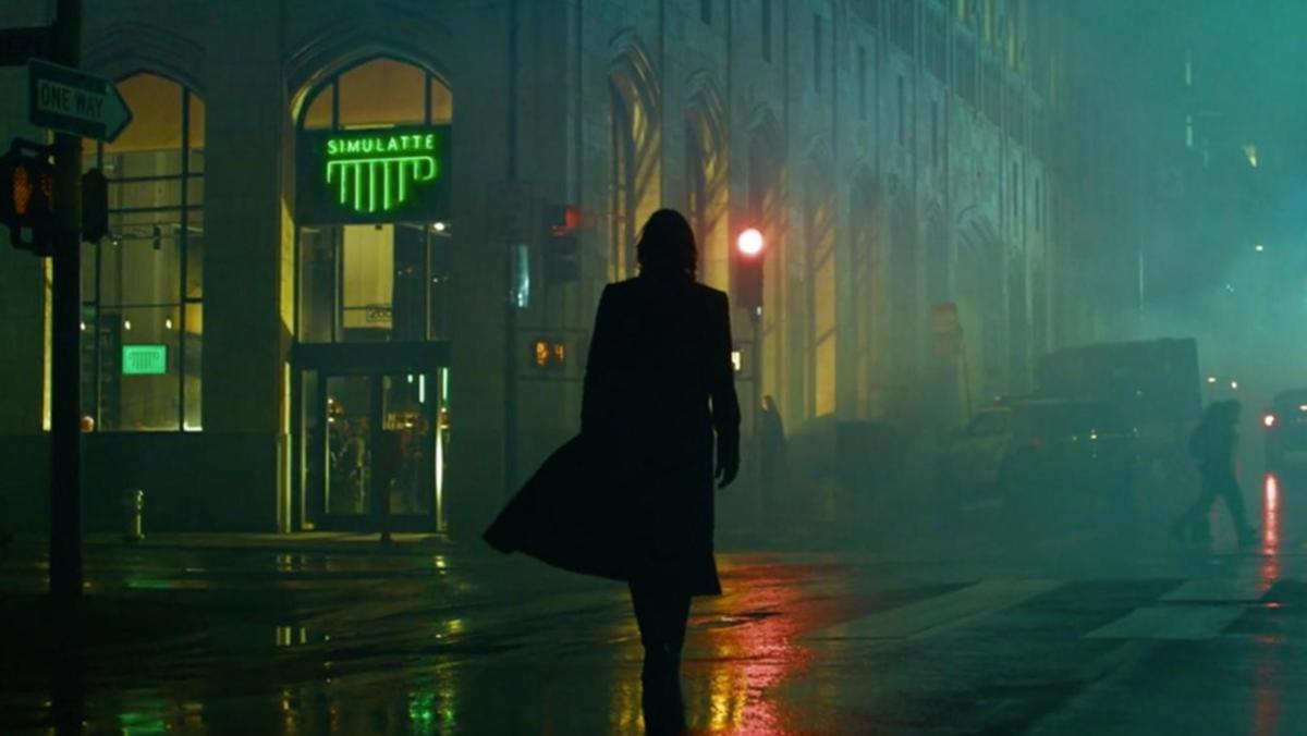 A still from the Matrix Resurrections shows Keanu Reeves as Neo in shadow walking towards a coffee shop called Simulatte